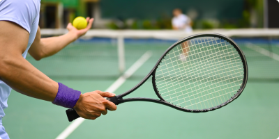Close view of player’s racket as he prepares to serve with his opponent in the distance.