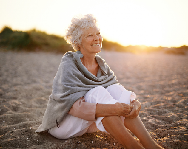 A senior woman sits on the beach at sunset