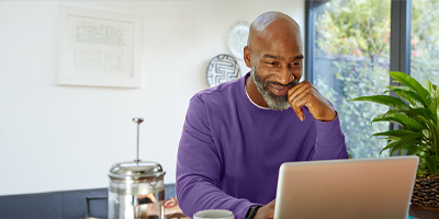 African American man in a purple sweater working on a laptop