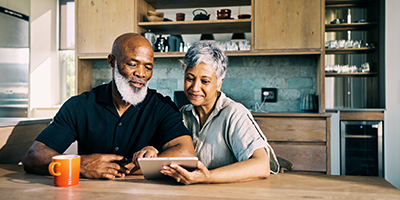 Older man and women sitting in kitchen looking at tablet screen.