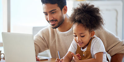 Dad working on his computer next to his daughter who is coloring