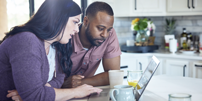A couple planning their financial future on their laptop in the kitchen over a cup of coffee.