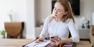 Woman in white shirt sitting at home on her mobile phone reviewing her 401(k).